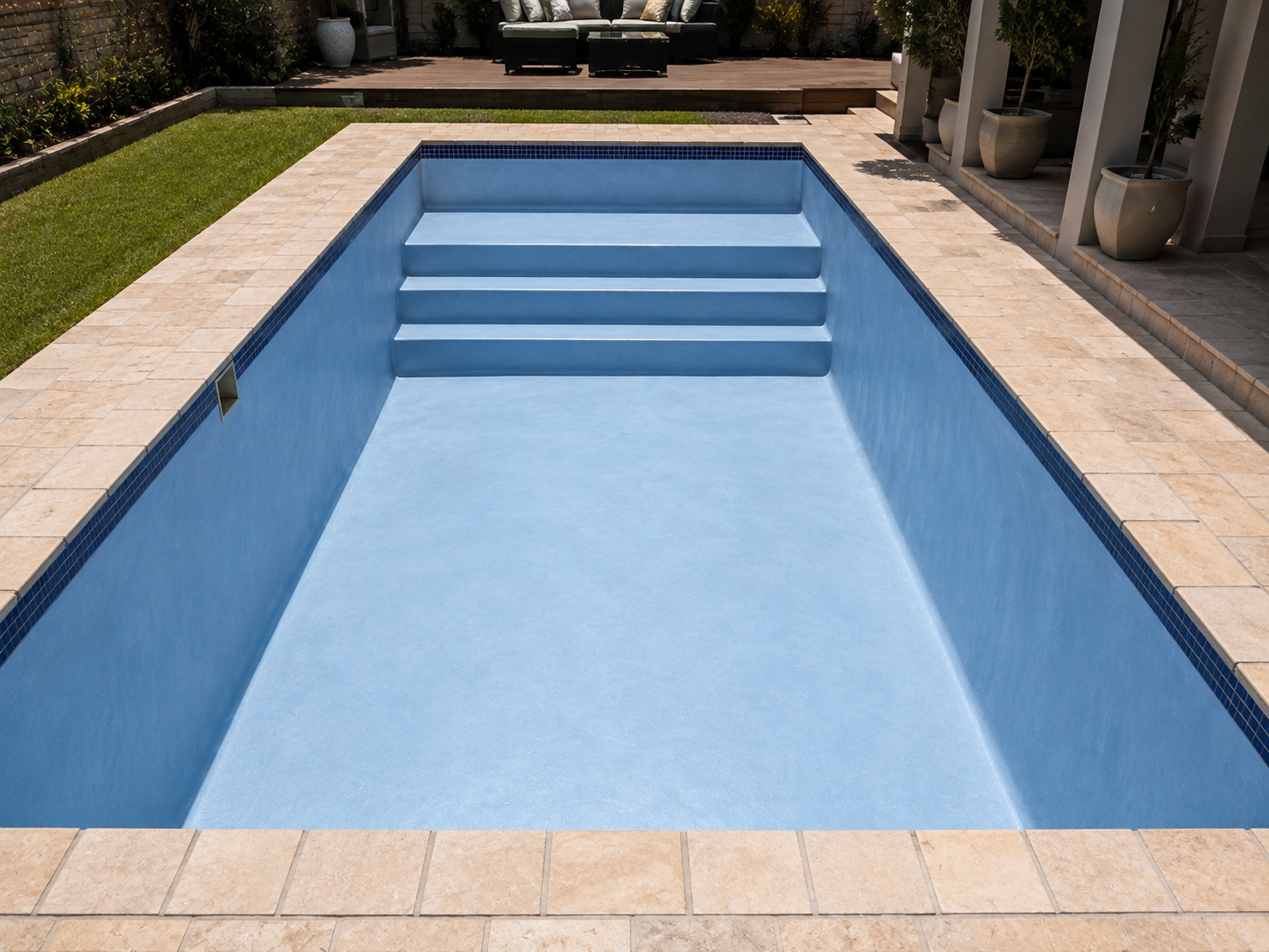 Freshly resurfaced rectangular pool with new blue interior finish, entry steps and travertine coping before refilling